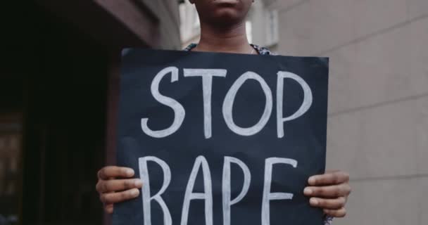 Vista de perto do ativista afro-americano segurando banner com slogan de estupro parada na rua da cidade. Menina de óculos apoiando movimento contra agressão. Conceito de problemas sociais . — Vídeo de Stock