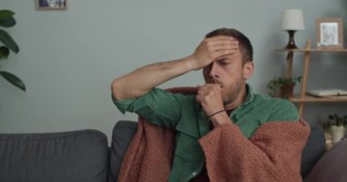 Sakallı adamın tedavi gördüğü ve öksürüğünün battaniyeye sarılı olduğu ekin manzarası. 30 'lu yaşlardaki hasta bir adam evdeki kanepede otururken kendini sağlıksız ve dokunaklı hissediyor. Hastalık kavramı.