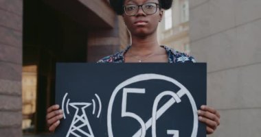 Afrika kökenli Amerikalı kadın aktivistin elinde 5 G işareti olmayan bir levha tutarken görüntüsü. Öğrenci kız yeni teknolojiye ve şehir caddesinde uygun anten konuşlanmasına karşı tek bir protesto yapıyor..