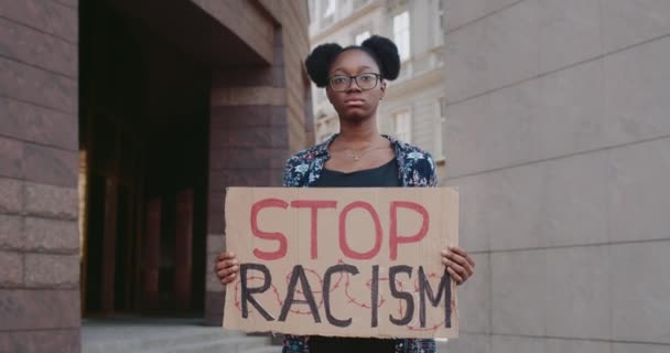 Afro-Amerikaanse meisje ondersteunen anti-racisme campagne in de stad straat.Jonge vrouwelijke estudent houden karton met stop racisme zin. Begrip gelijke mensenrechten en tolerantie. — Stockvideo