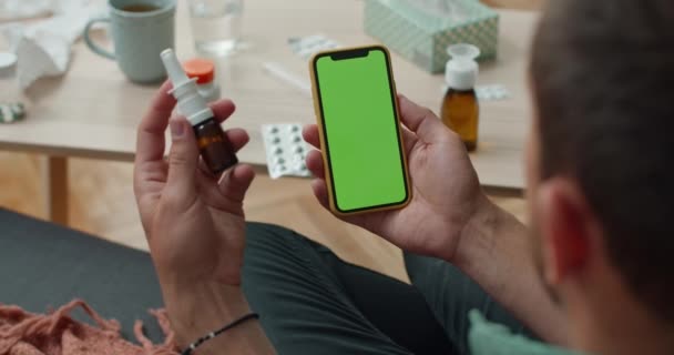 Sobre a visão do ombro da pessoa masculina usando mock up tela smartphone enquanto tem chamada de vídeo com o médico. Pessoa segurando gotas nasais enquanto consulta on-line. Conceito de telessaúde . — Vídeo de Stock