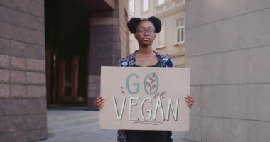Sokakta dururken elinde Go Vegan pankartı tutan Afrikalı Amerikalı bir kızın portresi. Vejeteryan yaşam tarzını kışkırtan gözlüklü bir kız öğrenci. Yeşil ve veganlık kavramı.