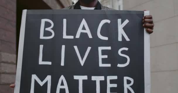 Close up view of african american guy holding banner with black lives matter writing. Male activist supporting movement against brutality and racism while standing at street. — Stock Video