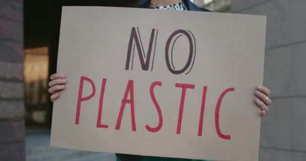 Zamknij widok żeńskich rąk trzymających kartonowe tabliczki bez plastikowego sloganu i stojących na ulicy miasta. Kobieta wspierająca ruch ekologiczny. Pojęcie zanieczyszczenia środowiska. — Wideo stockowe