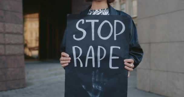 Närbild av kvinnliga händer håller banner med stopp våldtäkt skriva på stadens gata. Aktivist som stöder rörelse mot våld och misshandel. Begreppet sociala problem. — Stockvideo