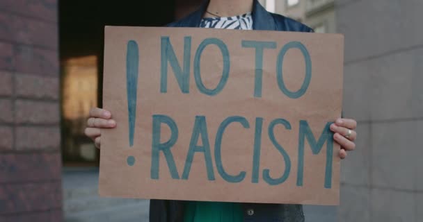 Vista de las cosechas de manos femeninas sosteniendo pancarta con no a la escritura racismo en la calle de la ciudad. Concepto de derechos humanos y desigualdad racial. — Vídeos de Stock