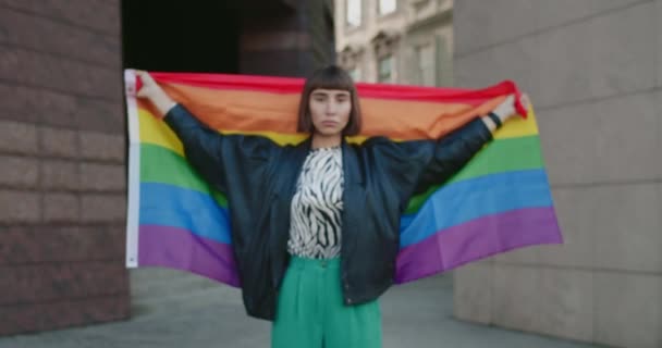 Portret poważnej dziewczyny przykrywającej się flagą lgbt patrząc w kamerę. Widok na milenijną lesbijkę stojącą na ulicy. Powiększ. Pojęcie dumy i LGBT . — Wideo stockowe