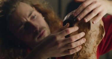 Çömlek kilinden insan kafası modelleyen konsantre milenyum adamının yakın görüntüsü. Erkek heykeltıraş sanatçı stüdyosunda büst yaratıyor. El yapımı sanat ve yaratıcılık kavramı.