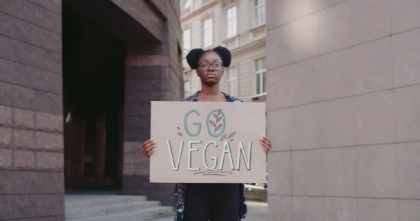 Mujer joven con Go signo vegano de pie en la calle de la ciudad y mirando a la cámara. Estudiante afroamericana que promueve el vegetarianismo y un estilo de vida saludable. Concepto de eco. Acercar. — Vídeos de Stock