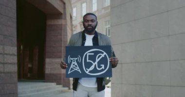 Genç Afro-Amerikan adam 5 G işareti olmadan pankart tutuyor. Ciddi sakallı adam 5G teknolojisini ve 5G uyumlu anten konuşlandırmasını protesto ediyor. Yakınlaştır.