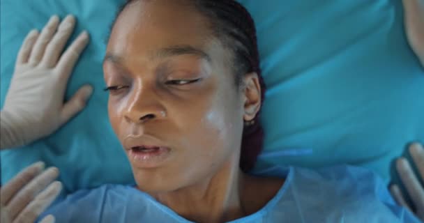 Girl lying on hospital stretcher while doctors transporting her to operating room. Top view of afro american woman opening eyes while going on ambulance to hospital. Concept of illness. — Stock Video