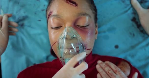 Afroamerikanerin mit Verletzungen und Sauerstoffmaske liegt im Krankenwagen auf einer Krankentrage. Nahaufnahme von Mädchen mit Blut und Wunden am Kopf Sanitäter transportieren in Klinik. — Stockvideo