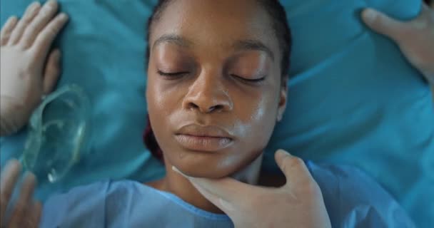 Hasta Afro-Amerikan kızı takan sağlık görevlileri oksijen solunum maskesiyle karşı karşıya. Hastaneye giderken tıbbi nakil sedyesinde yatan genç bir kadın. Hastalık kavramı. — Stok video