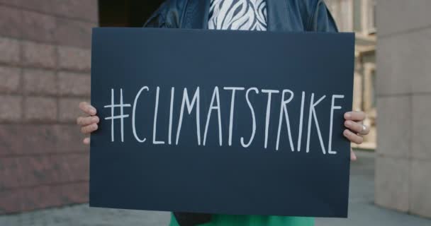 Manos femeninas sosteniendo cartel de cartón con etiqueta de huelga climática. Vista de cerca del activista que apoya el movimiento de conciencia ecológica mientras está parado en la calle de la ciudad. Concepto de salvar la Tierra. — Vídeo de stock