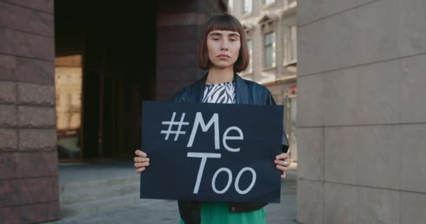 Egy fiatal nő portréja, aki transzparenssel a kezében ír és áll a város utcáján. Az orrkarikás lány támogatja a szexuális zaklatás elleni mozgalmat. A szociális problémák fogalma. — Stock videók