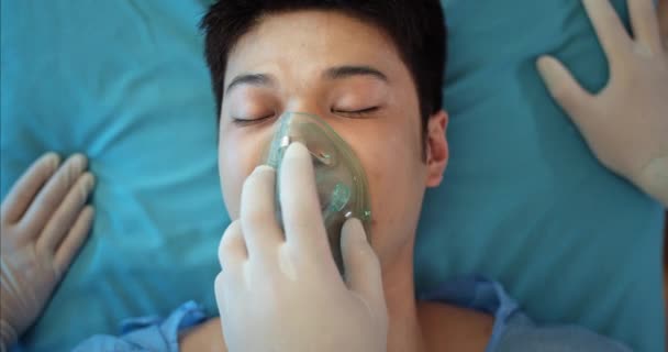 Detailní záběr mediků, jak si nasazují masku na dýchání kyslíku. Top pohled na podvědomé asijské chlap umírá při ležení na lékařské dopravní vozík na cestě do nemocnice. — Stock video