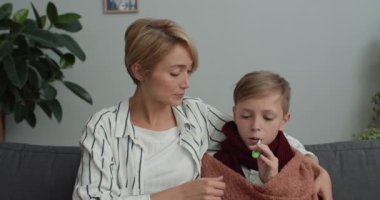 Genç annenin oğluyla konuştuğu ve ona termometre verdiği görüntüler. Aile, doktorla çevrimiçi tıbbi danışmanlık yaparken kameraya bakıyor..