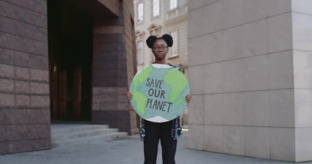 Афро-американка, держащая модель Земли с надписью, спасает нашу планету. Серьезные девушки борются с загрязнением окружающей среды, стоя на улице. Концепция экологического движения. Увеличь. — стоковое видео