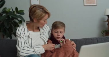 İnternette tıbbi danışmanlık yaparken dizüstü bilgisayara bakan kadın ve hasta çocuk görüntüsü. Anne konuşuyor, termometreyi veriyor ve video ararken doktorlara hapları gösteriyor..