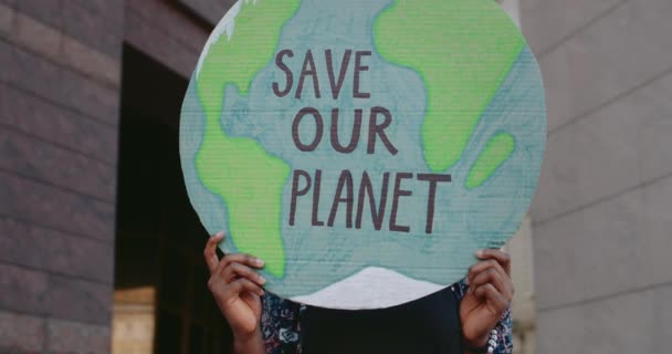 Vista de la cosecha de la persona afroamericana sosteniendo el modelo de la Tierra con la escritura salvar nuestro planeta. Manos femeninas sosteniendo cartel mientras golpean contra la polución ambiental. Concepto de ecología. — Vídeo de stock