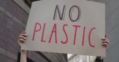 Kadın ellerinin plastik slogan kullanmadan karton levhayı kaldırdığı ve şehir caddesinde durduğu yakın plan. Ekoloji hareketini destekleyen kadın. Çevre kirliliği kavramı.