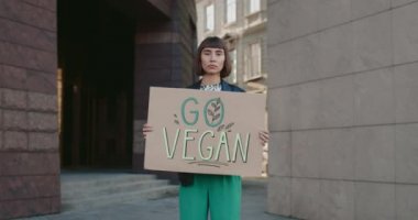 Elinde Go vegan tabelası olan genç bir kız boş caddede kameraya bakıyor. Kadın hipster vejetaryenliği ve sağlıklı yaşam tarzını destekliyor. Go Green ve Eko kavramı. Yakınlaştır.