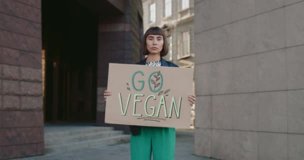 Молодая девушка с веганским знаком Го стоит на пустой улице и смотрит в камеру. Женщины-хипстеры пропагандируют вегетарианство и здоровый образ жизни. Озил из Go Green и eco. Увеличь. — стоковое видео