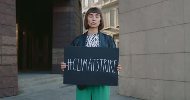 Millennial-Frau mit Plakat mit Klimastreik-Hashtag, während sie auf der Straße steht. Hipster-Mädchen streiken für Ökologie und sauberen Planeten. Konzept von Öko und Erde retten. Vergrößern. — Stockvideo