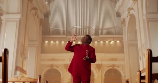 Genç Afrikalı Amerikalı adam ibadet şarkısı söylüyor. Kırmızı takım elbiseli erkek şarkıcı kilisede dururken duygusal ve hareketli eller yapıyor. İnsan ve müzik kavramı. — Stok video