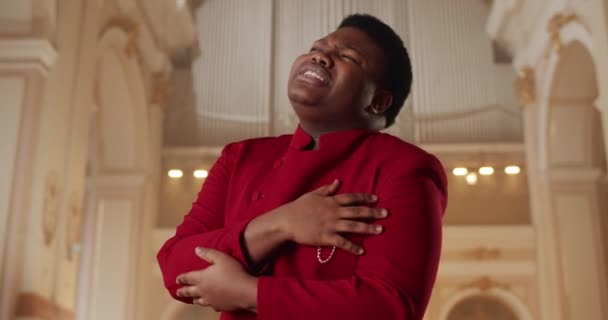 Afro american male preacher singing gospel music. Young man in 30s wearing red suit performing emotionally and moving hands while standing in church. Concept of people and religion. — Stock Video