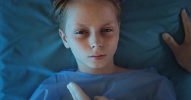 Vista superior del niño tendido en el carro de transporte mientras paramédico revisa el pulso. Vista de cerca del niño enfermo mirando a la cámara mientras viaja en ambulancia al hospital. Concepto de asistencia sanitaria. — Vídeo de stock