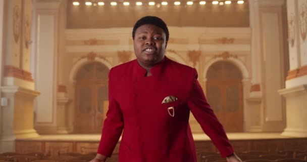 Front view of young african american man singing gospel music. Male singer in red suit performing emotionally and moving hands while standing in church. Concept of people and religion. — Stock Video