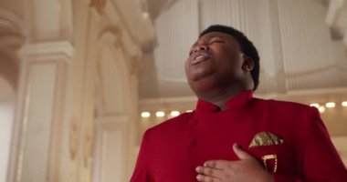 30 'lu yaşlarda Afro-Amerikan erkek gospel şarkıcısı. Kırmızı takım elbiseli bir adamın dua evinde dururken ruhani müzik söyleyişini yakından izleyin. Din ve insan kavramı.