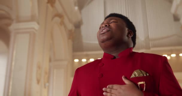 Afro american male gospel singer in 30s. Close up view of man wearing red suit singing spiritual music while standing in house of prayer. Concept of religion and people. — Stock Video