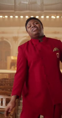 Neşeli Afro-Amerikan gospel şarkıcısı ahşap sıralarda duruyor ve şarkı söylüyor. Genç adam kameraya bakarken ibadet müziği yapıyor ve elleri ritimle hareket ettiriyor..