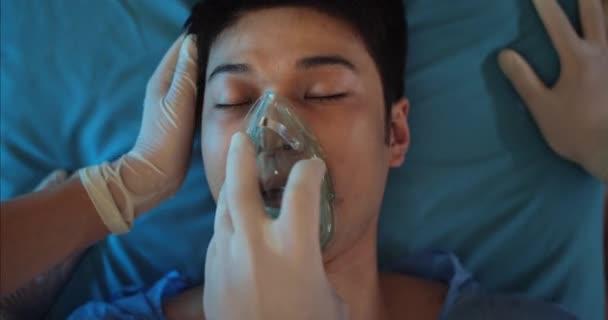 Detailní záběr zdravotníků, jak si nasazují masku na dýchání kyslíku. Asiat v bezvědomí leží na nosítkách, když jde do nemocnice. Pojem nemoci. — Stock video