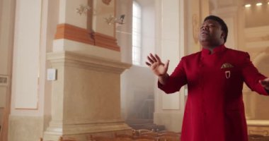 30 'lu yaşlarda Afro-Amerikan erkek gospel şarkıcısı. Kırmızı takım elbiseli genç adam dua evinde ruhani müzik söylerken ellerini hareket ettiriyor. Din ve insan kavramı.