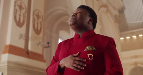 Crop view of african american male gospel singer in 30s. Young man wearing red suit putting hand on heart while singing spiritual music in house of prayer. Concept of religion and people. — Stock Video