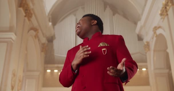 Vue du bas du jeune chanteur homme émotionnel portant en costume rouge. Chanteur de gospel spirituel masculin chantant hymne et mains en mouvement. Concept de religion et de peuple. — Video