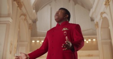 Afro-Amerikalı bir adamın kilisede gospel müziği söylemesi. Kırmızı elbiseli duygusal erkek şarkıcının portresi kilisede duruyor ve el sıkışıyor. Din kavramı ve insanlar..