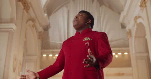 Портрет эмоционального певца в красном костюме, стоящего в церкви и двигающего руками.. — стоковое видео
