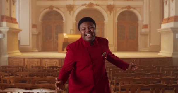 Crop view of gospel singer in red suit looking to camera and singing while standing at row of wooden church pews. Young guy performing worship music and moving hands in rhytm in church. — Stock Video