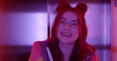 Kafasını çevirip kameraya bakan güzel bayan kulüp üyelerine yakın çekim. Neşeli bin yıllık kadın portresi neon ışıklarda dururken gülümseyen ve elleriyle yüzünü destekleyen..