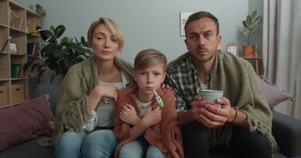 Sick family sitting on couch while having online medical consultation at home. Mother, father and child boy looking to camera while communicating with doctor. Concept of telehealth. — Stock Video