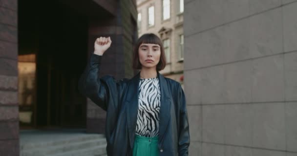 Jovem mulher atraente levantando a mão com o punho apertado enquanto está de pé na rua. Milenar ativista apoiando movimento e lutando pelos direitos humanos. Conceito de protesto. — Vídeo de Stock