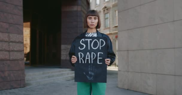 Серьёзная молодая девушка с плакатом о прекращении изнасилования на городской улице. Женщина-активистка с кольцом в носу поддерживает движение против насилия и нападения. Концепция социальных проблем. — стоковое видео