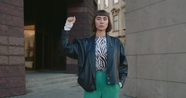 거리에서 서 손가락을 꽉 쥐고 손을 든 매력적 인 젊은 여자. 밀레니엄걸 운동가는 운동을 지지하고 인권을 위해 싸우고 있습니다. 항의 개념. — 비디오