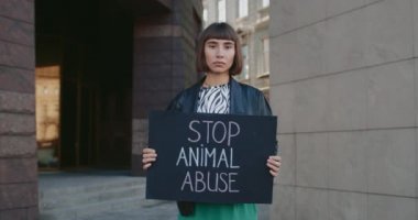 Milenyum yeniyetme kız elinde hayvan istismarı yazılarını durduran bir karton levha tutuyor. Sokakta kameraya bakan kadın hayvan hakları savunucusunun portresi. Sosyal sorun kavramı.