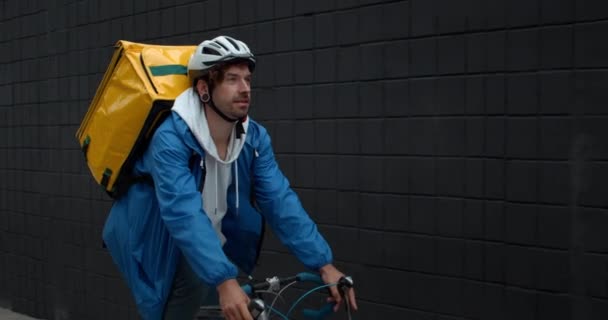 Молодой курьер с рюкзаком для перевозки еды на велосипеде на улице. Человек в защитном велосипедном шлеме доставляет заказ клиенту. Концепция доставки продуктов питания. — стоковое видео
