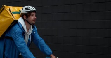 Bisikletli kurye, sokakta omzunda yiyecek taşıma çantasıyla bisiklete biniyor. Koruyucu bisiklet kasklı adam müşteriye sipariş getiriyor. Yemek dağıtım servisi kavramı.